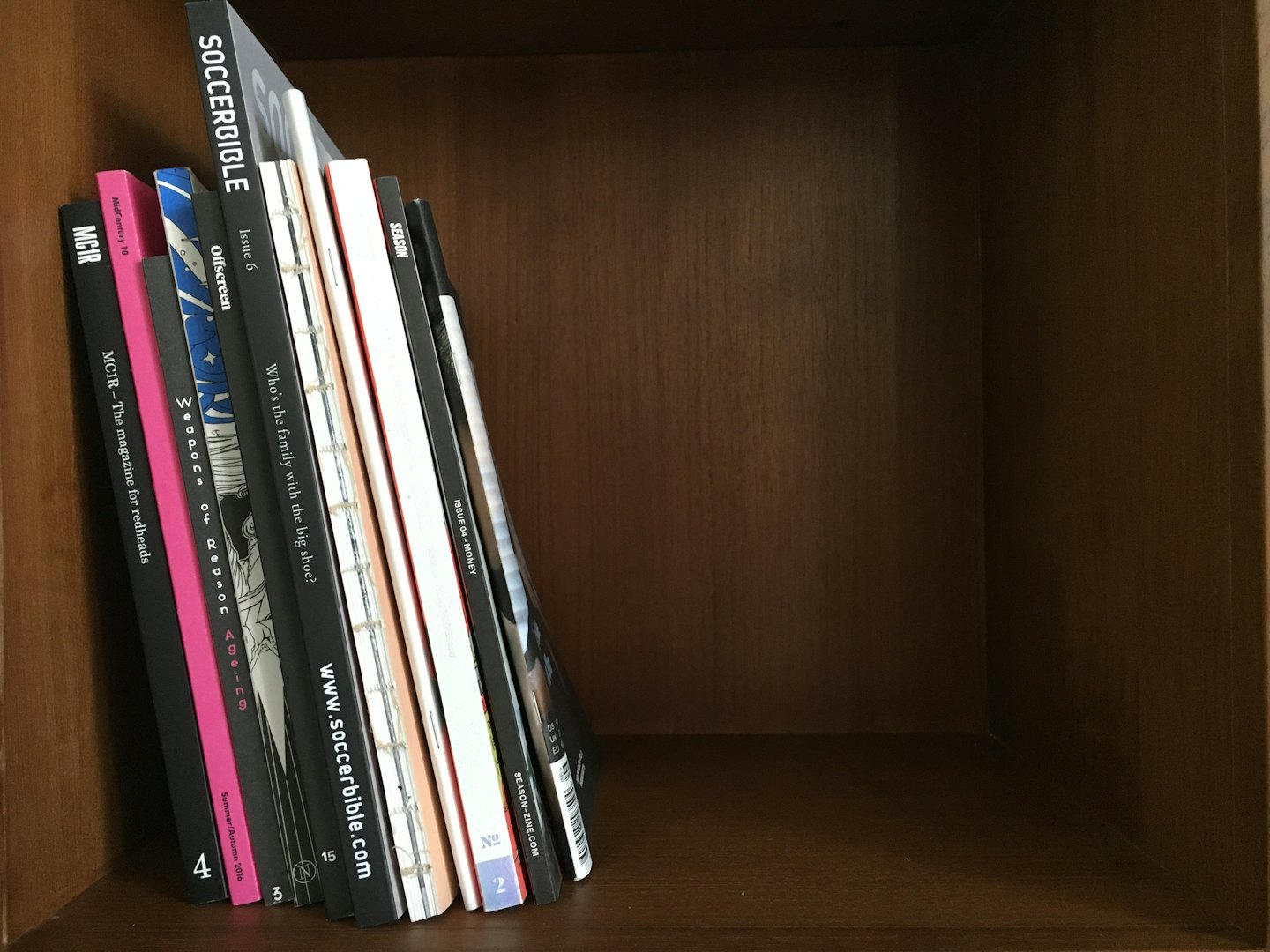 Una pila di riviste e fanzine diverse su una libreria di legno.