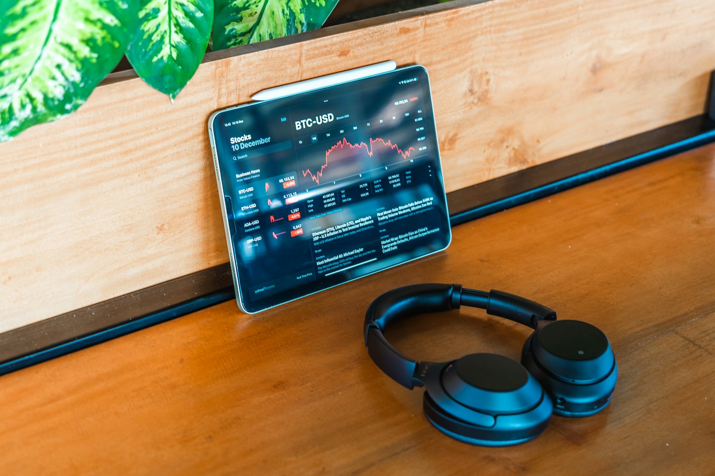 Tablet con grafici di criptovalute, cuffie e pianta.