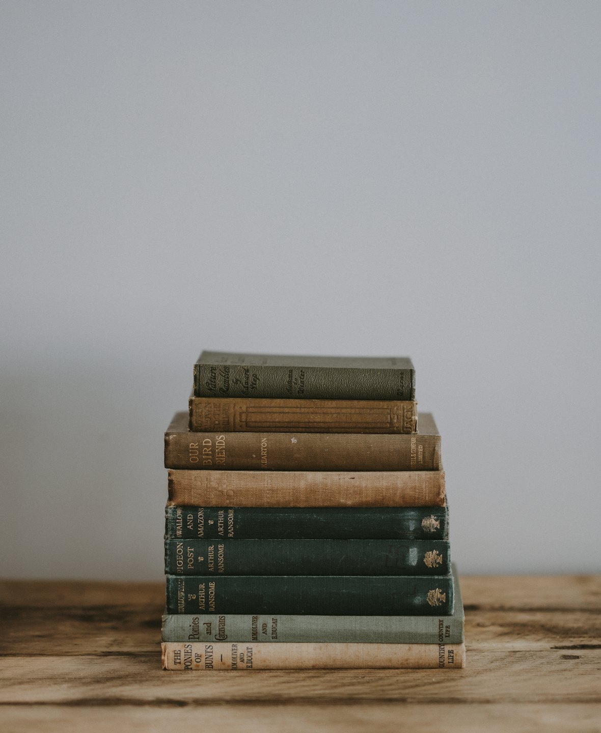 Libri antichi impilati con copertine verdi e marroni sbiadite su un tavolo di legno.